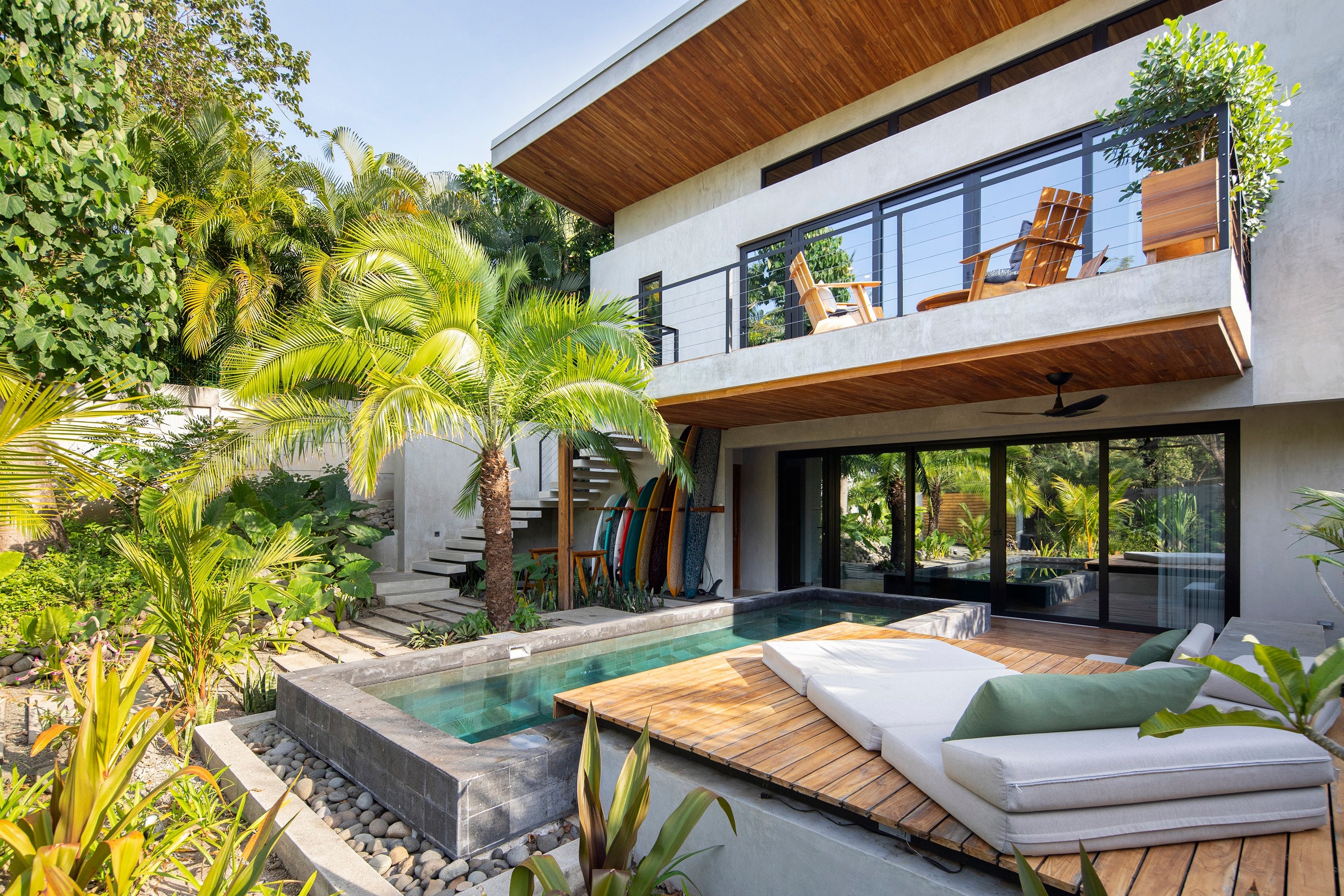 Two-storey house with large windows, a pool and a tropical garden.