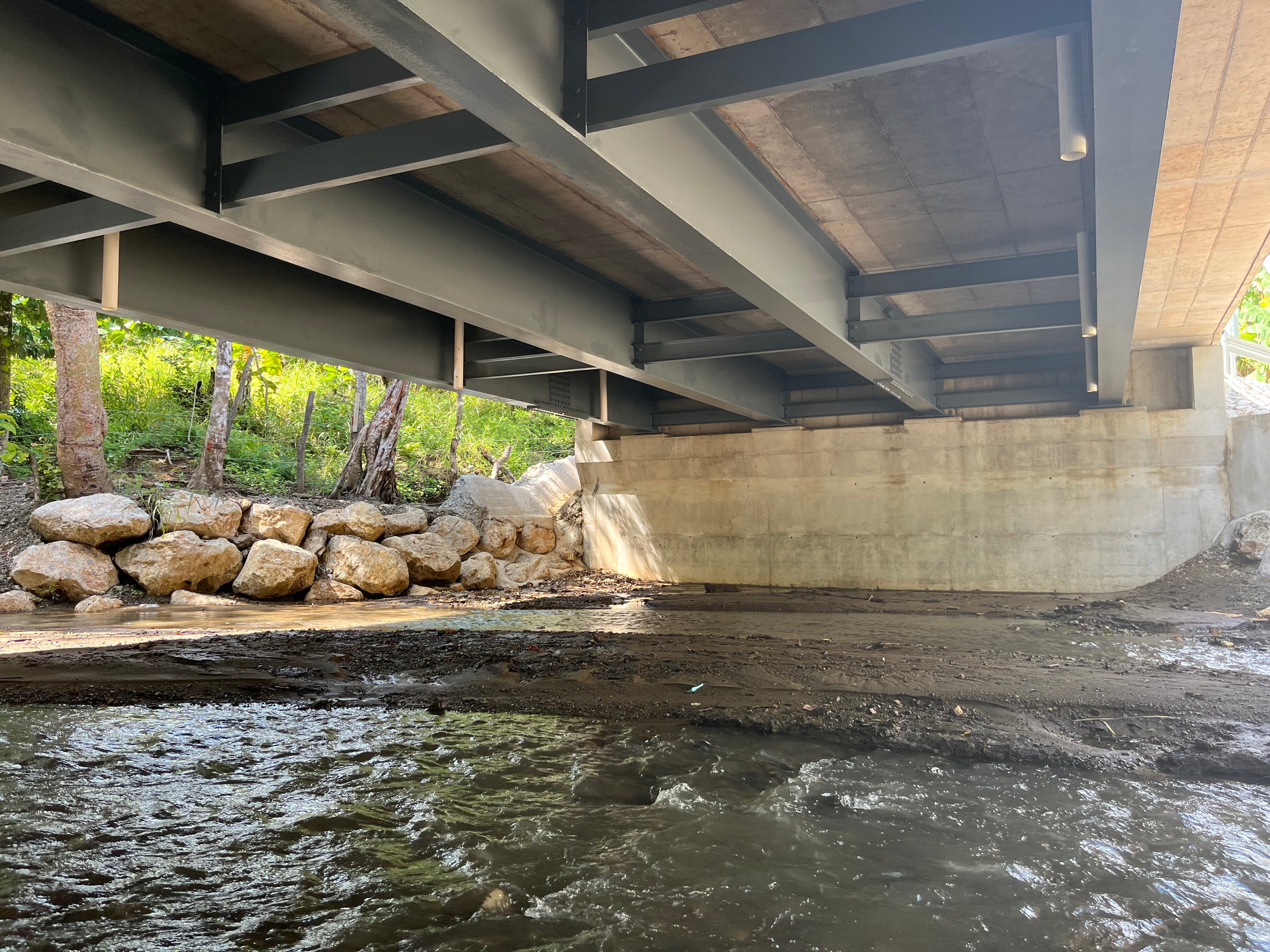 Steel girders of a bridge over a rocky streambed.