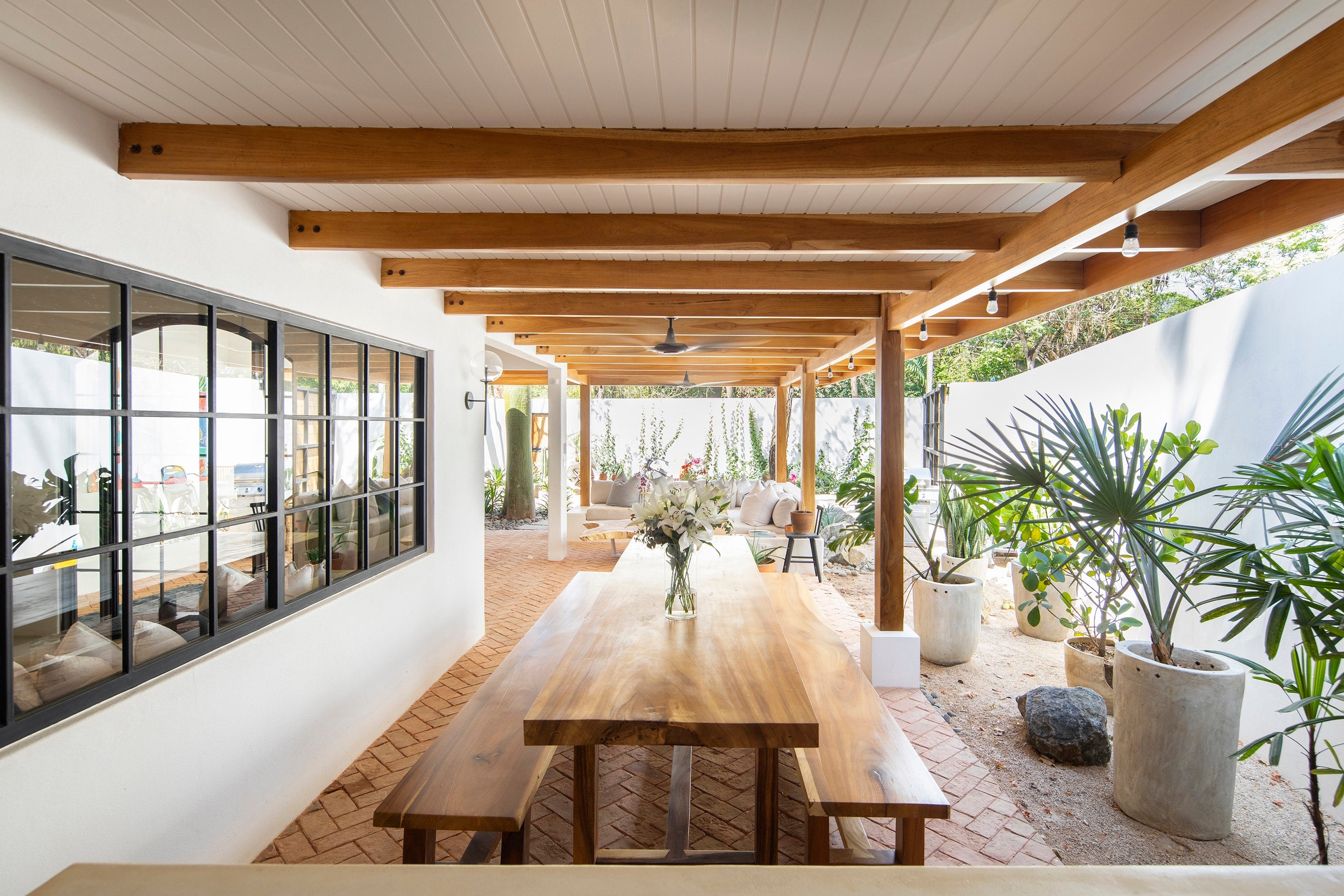 Terraza techada con vigas y columnas de madera sobre una mesa de comedor larga