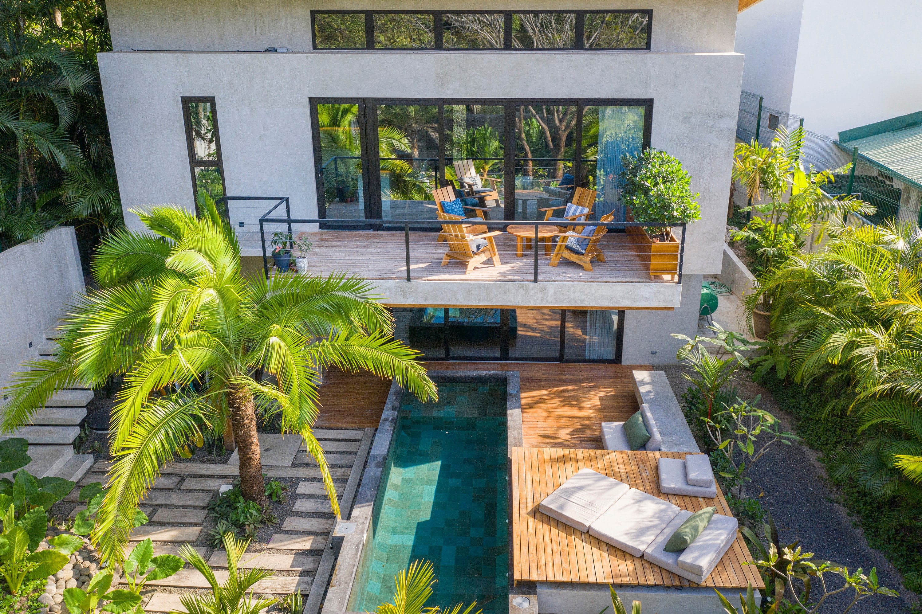 Casa de dos niveles con grandes ventanales, piscina y jardín tropical