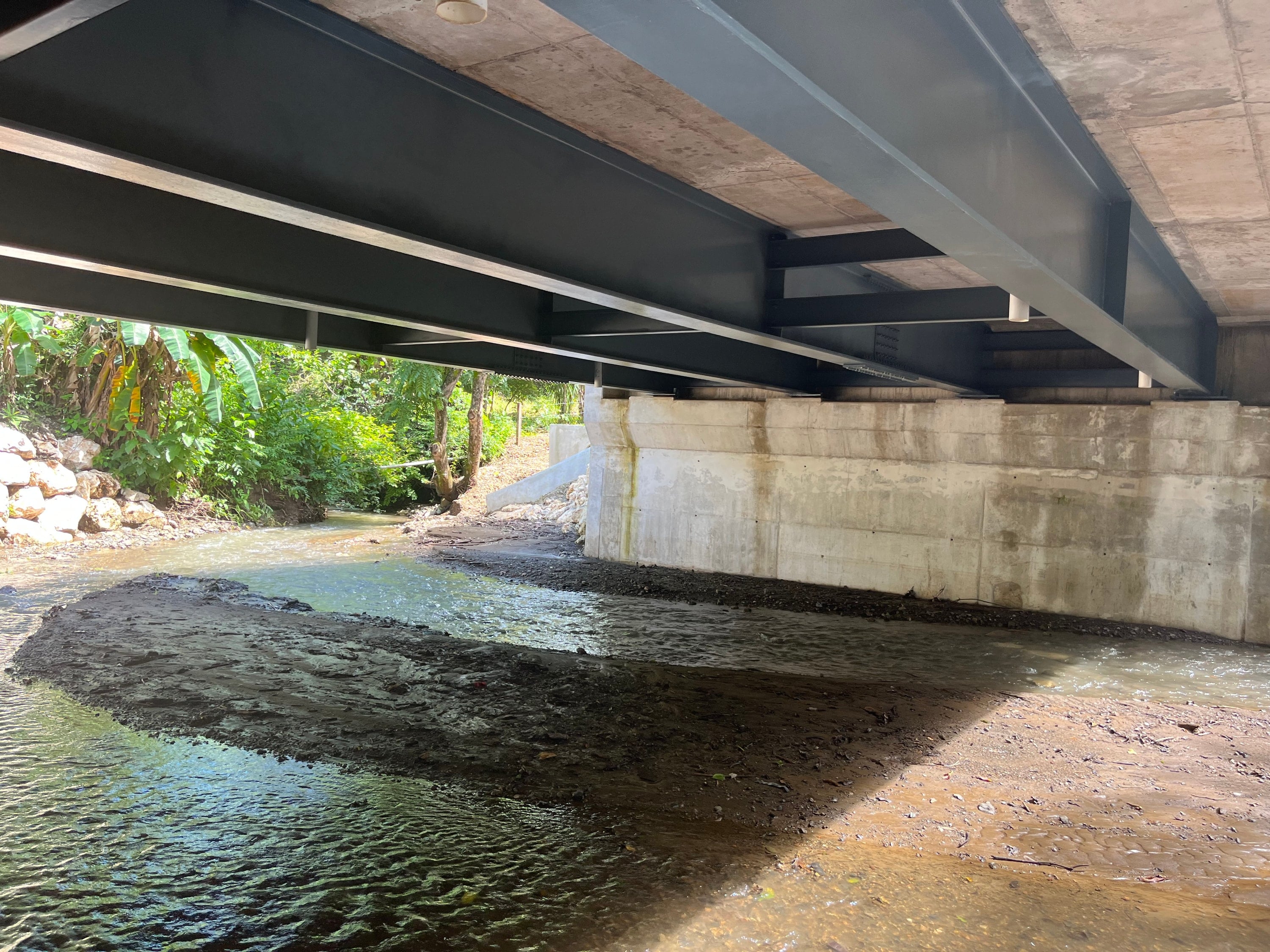 Steel girders of a bridge over a rocky streambed.