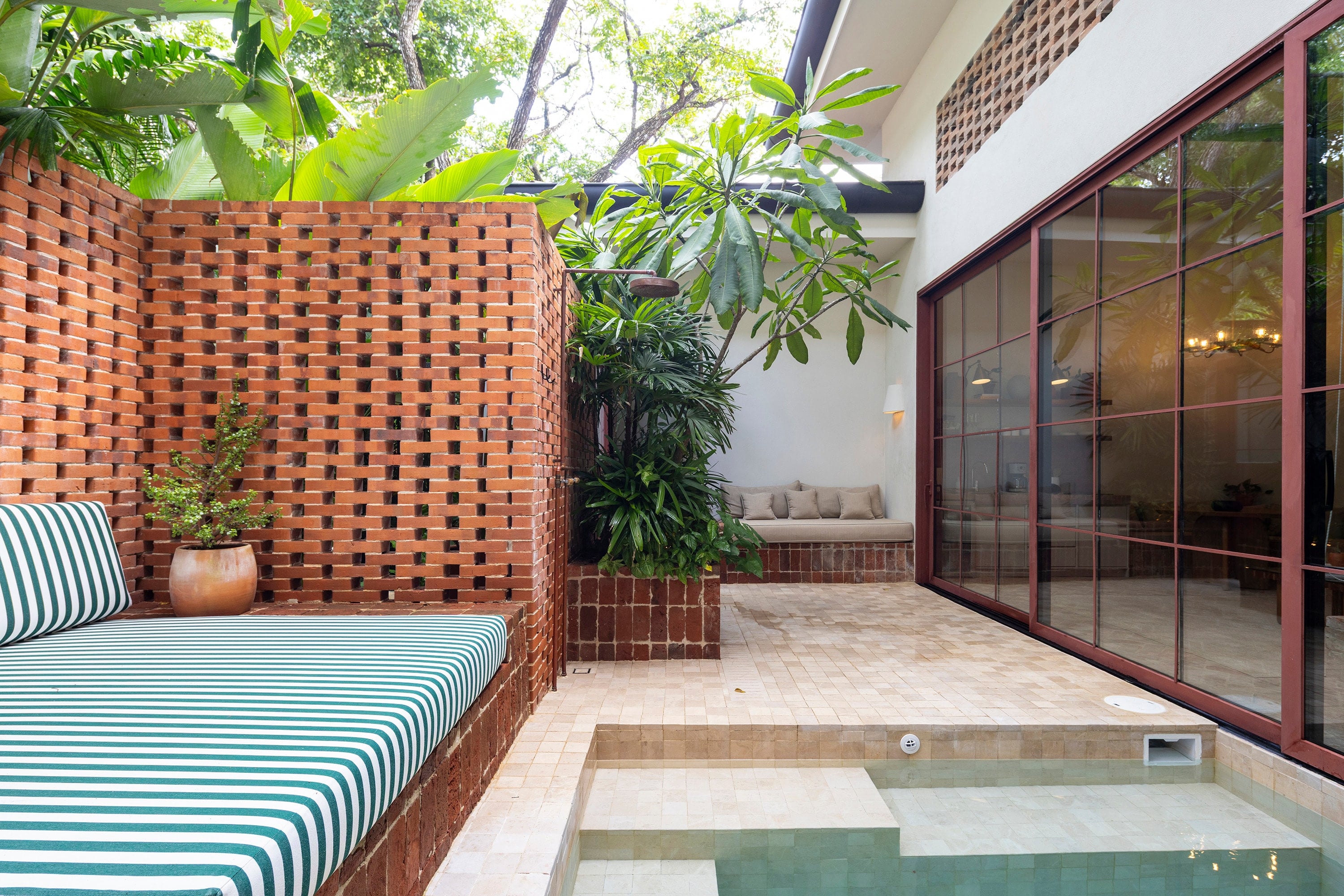 Patio con celosía de ladrillo y una pequeña piscina rodeada de vegetación.